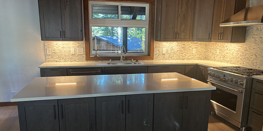 Bright kitchen with white and dark green cabinetry, featuring a farmhouse sink, stainless steel refrigerator, and a marble-like countertop.