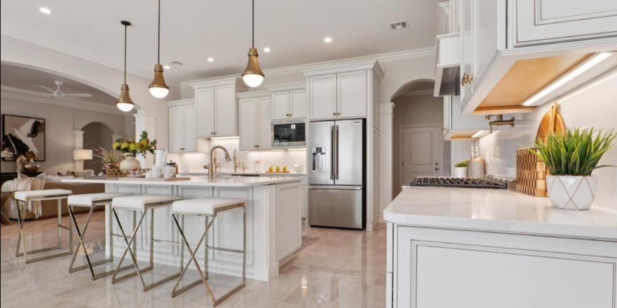 Bright kitchen with white and dark green cabinetry, featuring a farmhouse sink, stainless steel refrigerator, and a marble-like countertop.