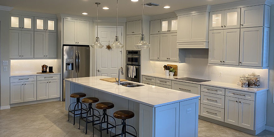 A bright kitchen with white cabinetry, a large marble island, and stainless steel appliances.