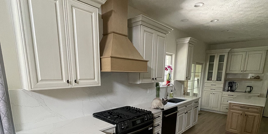 Bright kitchen with white and dark green cabinetry, featuring a farmhouse sink, stainless steel refrigerator, and a marble-like countertop.