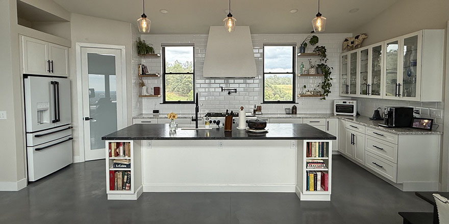 A bright kitchen with white cabinetry, a large marble island, and stainless steel appliances.