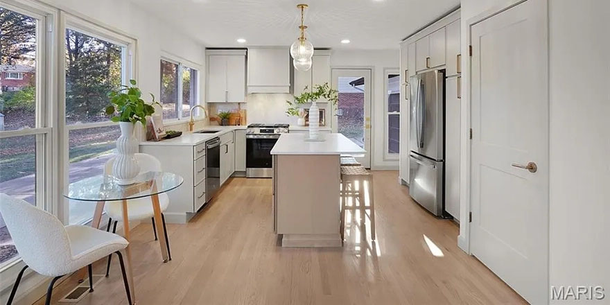 A bright kitchen with white cabinetry, a large marble island, and stainless steel appliances.