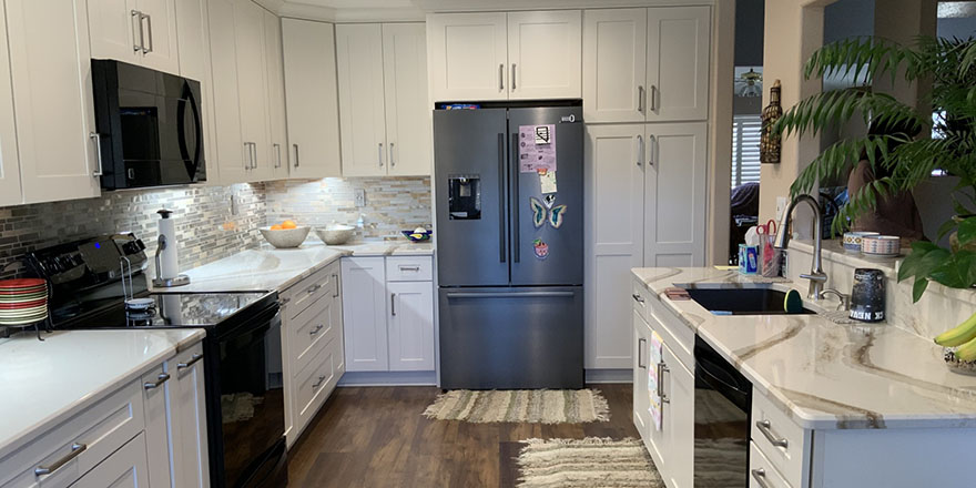 Bright kitchen with white and dark green cabinetry, featuring a farmhouse sink, stainless steel refrigerator, and a marble-like countertop.
