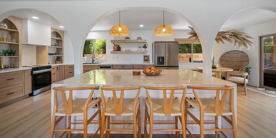 A bright kitchen with white cabinetry, a large marble island, and stainless steel appliances.