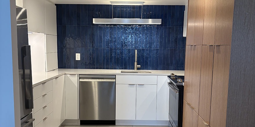 Bright kitchen with white and dark green cabinetry, featuring a farmhouse sink, stainless steel refrigerator, and a marble-like countertop.