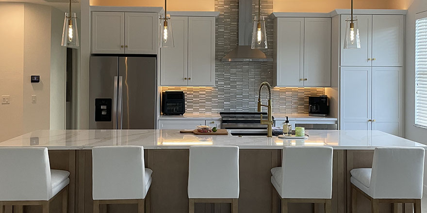 A bright kitchen with white cabinetry, a large marble island, and stainless steel appliances.