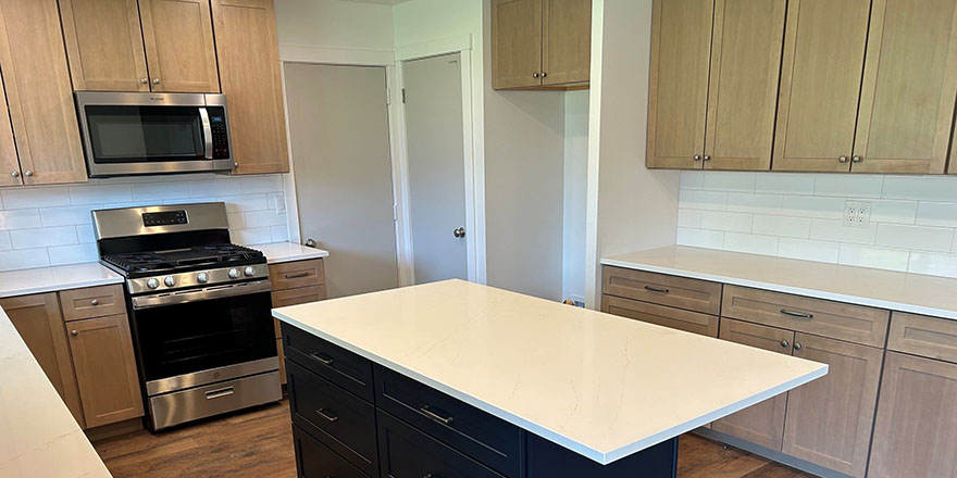 Bright kitchen with white and dark green cabinetry, featuring a farmhouse sink, stainless steel refrigerator, and a marble-like countertop.
