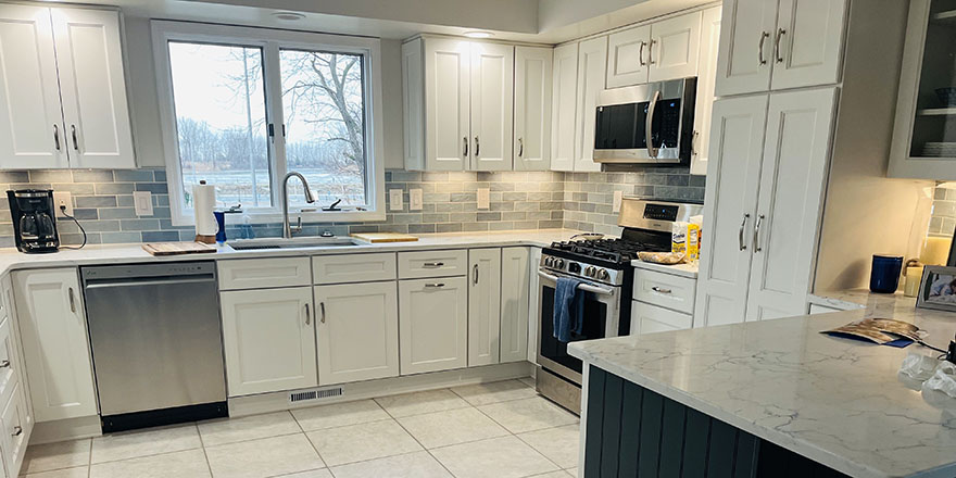 A bright kitchen with white cabinetry, a large marble island, and stainless steel appliances.